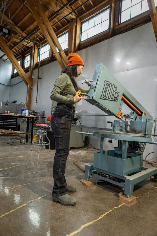 Woman wearing the Dovetail Beanie in Paprika while operating machinery in a workshop, demonstrating the work-ready style of Dovetail Workwear's cuffed beanie design