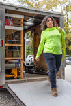 Woman exiting a mobile workshop trailer wearing Dovetail Workwear's Christa DIY Pant in Sulfur Navy with a bright neon yellow pullover and work boots
