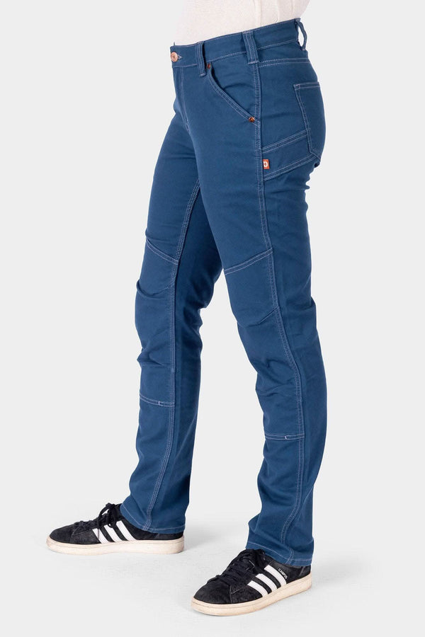 Side view of a woman wearing Dovetail Workwear GO TO™ Stretch Canvas Pant in Atlantic Blue, highlighting articulated knee and straight leg fit with black and white sneakers