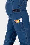 Side view of a woman wearing Dovetail Workwear GO TO™ Stretch Canvas Pant in Atlantic Blue, displaying nested pockets holding a snack and phone, with tool loop visible on thigh