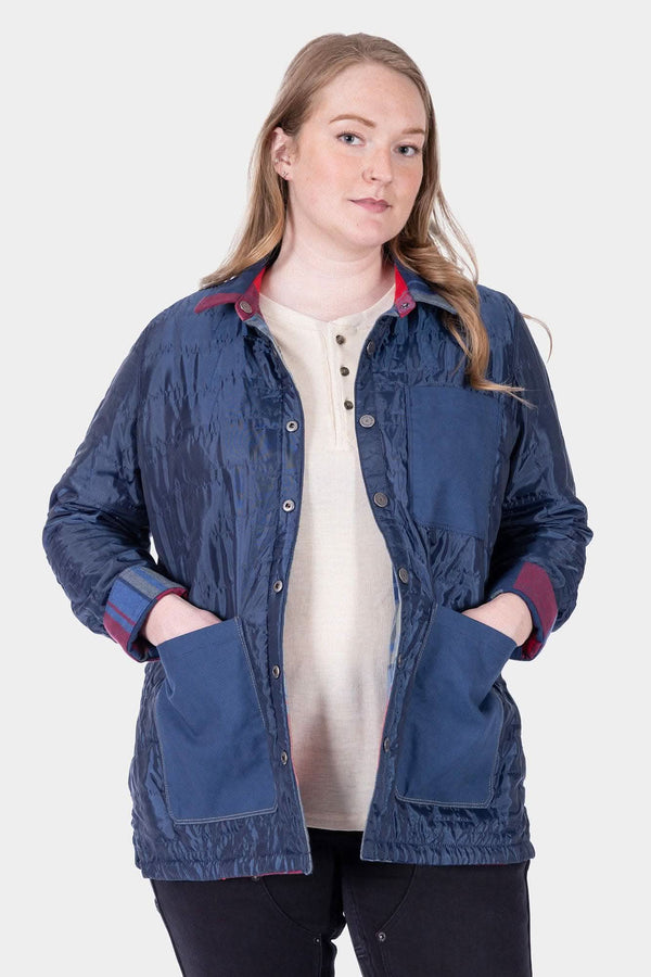 Woman wearing the Dovetail Workwear Durham Reversible Quilted Shirt Jac in Loden Green Plaid with Barn Red Plaid lining visible at collar and cuffs, hands in pockets
