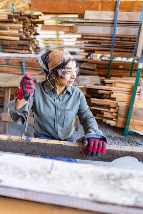 Woman wearing the Givens Stretch Chamois Work Shirt in Patina Green by Dovetail Workwear, demonstrating the shirt's stretch and comfort in a woodworking setting