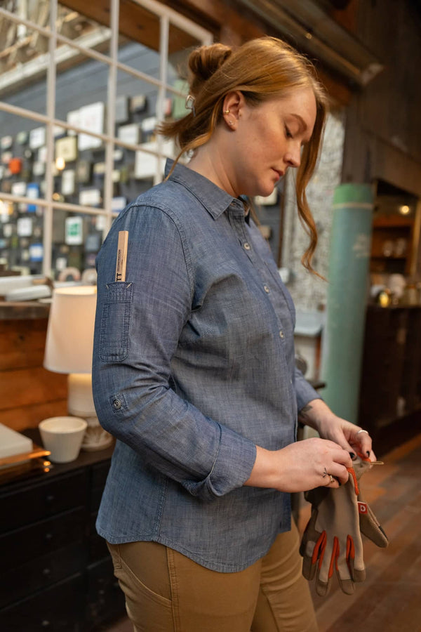 Side view of a woman wearing the Indigo Blue Givens Long Sleeve Summer Work Shirt by Dovetail Workwear, featuring the visible chest pocket and pencil pocket on sleeve