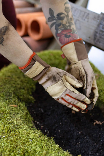 Dovetail Workwear Performance Work Gloves in Light Kodiak being worn while gardening, showing genuine leather protection and breathable stretch panels with adjustable wrist strap