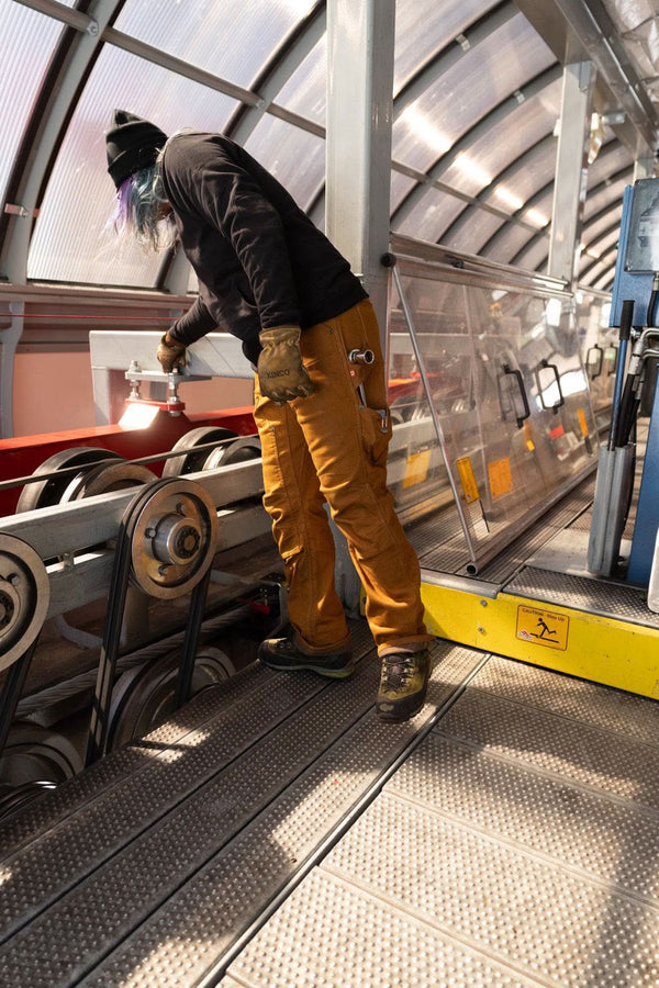 Woman wearing Dovetail Workwear GO TO™ Hoodie in Carbon Black with reinforced elbows, working in industrial setting with polycarbonate overhead panels
