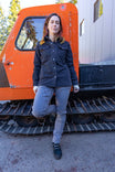 Woman in black Oahe HOTSWAP™ Thermal Denim Work Jacket by Dovetail Workwear leaning against orange vintage truck cab outdoors