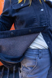 Detail view of the Dovetail Workwear Oahe HOTSWAP™ Thermal Denim Work Jacket in Black, showing the brushed thermal lining and zip closure on a woman wearing layered clothing