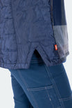 Detail view of the Durham Reversible Quilted Shirt Jac by Dovetail Workwear showing quilted exterior with reinforced side seam and visible orange brand label on woman wearing denim jeans