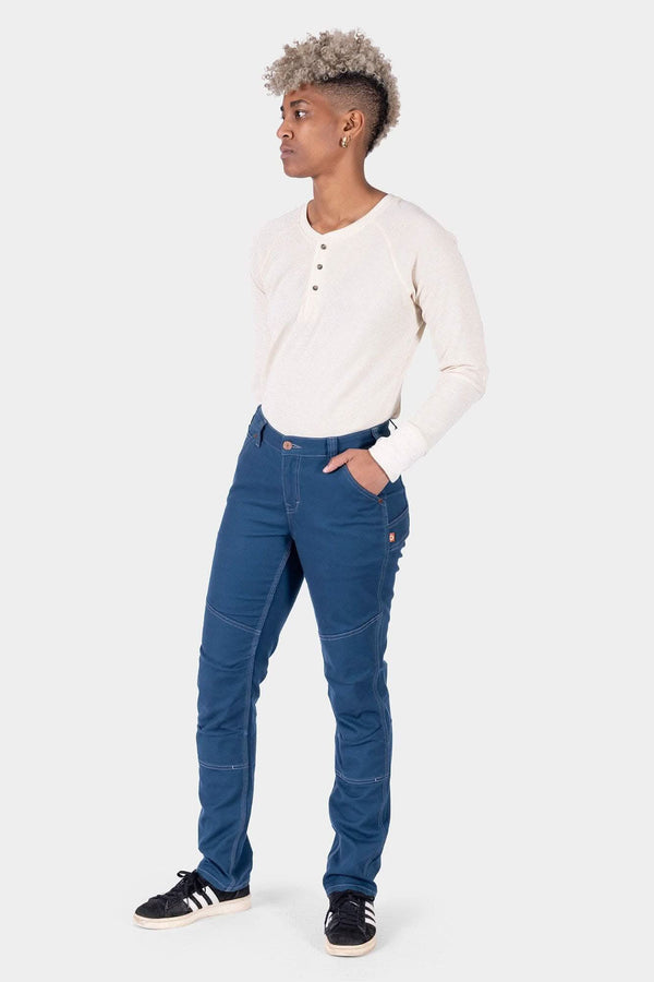 Side view of a woman wearing Dovetail Workwear's GO TO™ Stretch Canvas Pant in Atlantic Blue with a cream henley, showcasing the straight leg fit and articulated knee design