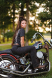 Back view of a woman sitting on a Harley-Davidson motorcycle wearing John Deere X Dovetail Workwear Into Town Bootcut Jeans in Classic Black