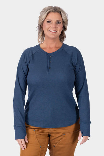 Dovetail Workwear's Honed Long Sleeve Thermal Henley in Atlantic Blue, shown on a woman wearing caramel pants, featuring a button placket and reinforced elbows