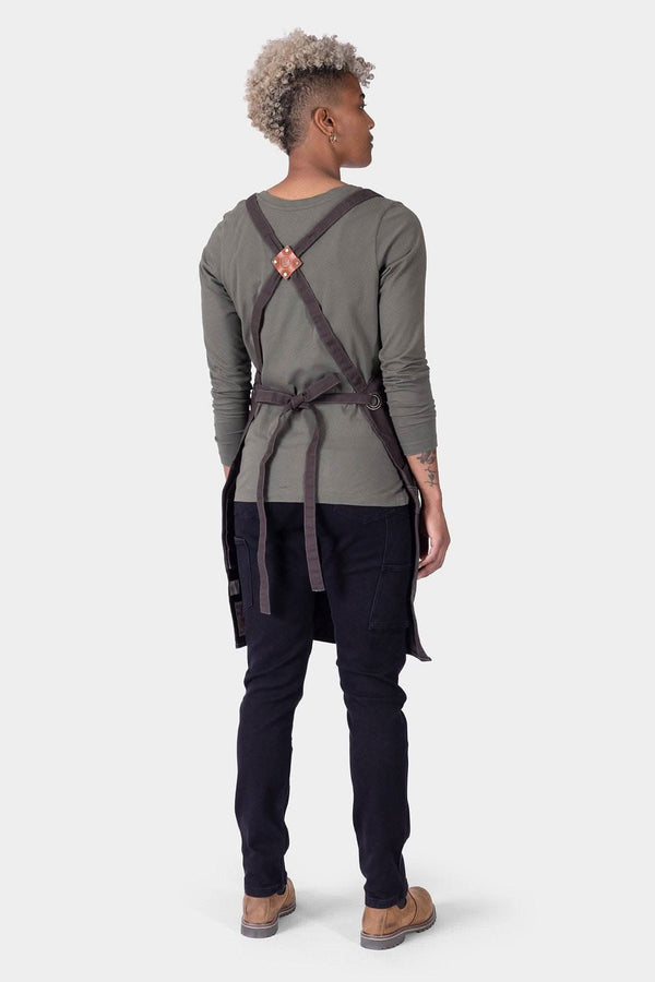 Back view of a woman wearing the Dovetail Workwear Obana Work Apron in Dark Blue Wabash Stripe, showing cross-back straps and multiple pockets