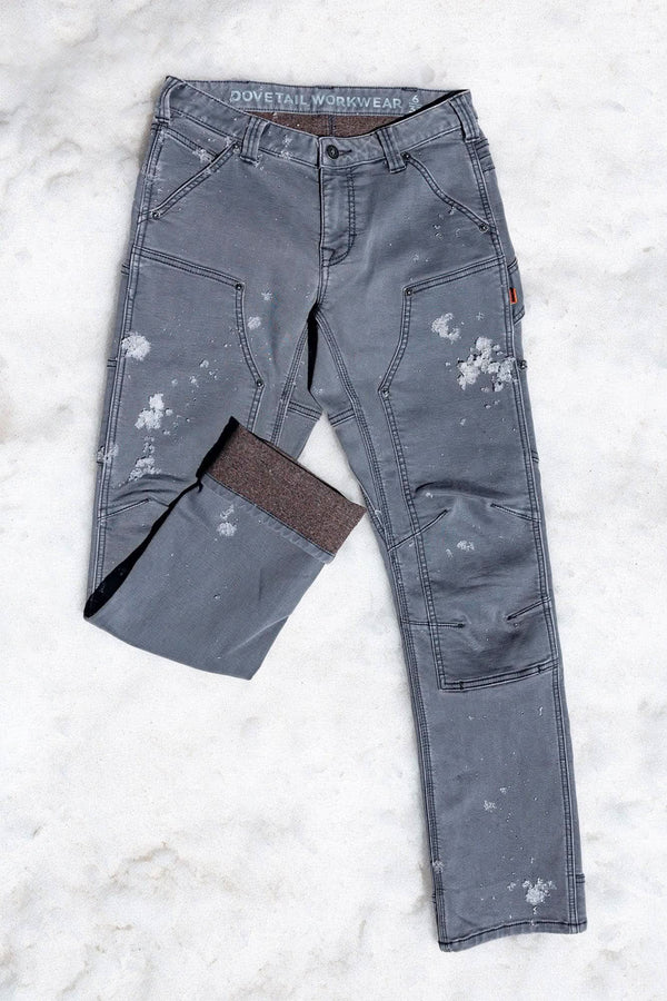 Flat lay of Dovetail Workwear's Britt Utility HOTSWAP™ Pant in Grey Thermal Denim, displaying cargo-style pockets, tool loop, and thermal fabric with paint splatters from work use