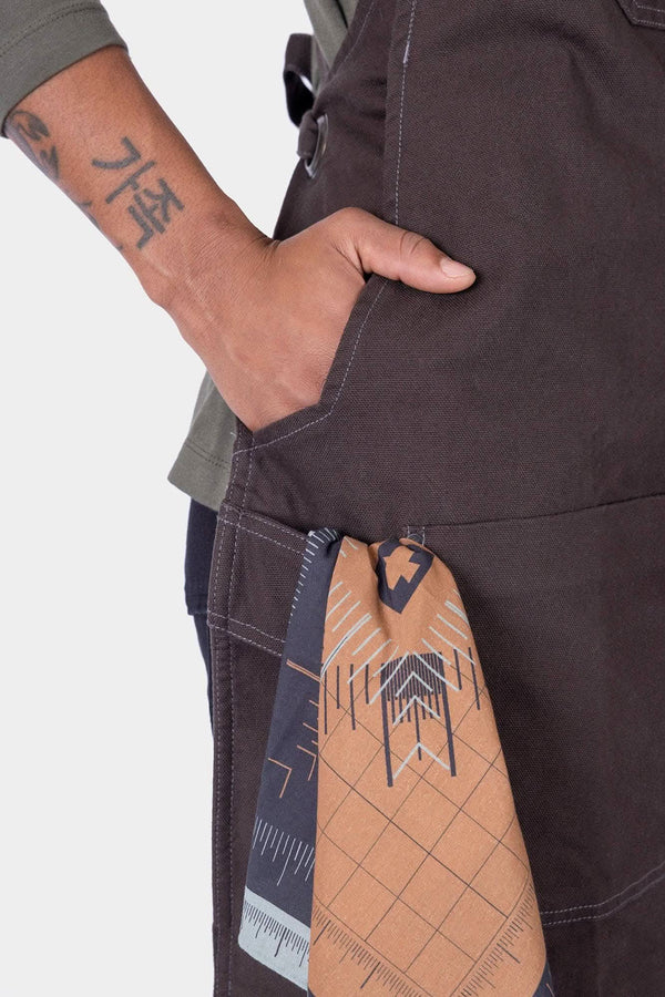 Detail view of a woman's hand in the pocket of the Kodiak Brown Obana Work Apron by Dovetail Workwear, showcasing the functional pocket design