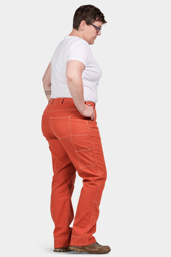 Side view of a woman wearing Dovetail Workwear Anna Taskpant in Paprika Orange canvas, showcasing the relaxed leg fit and nested pockets