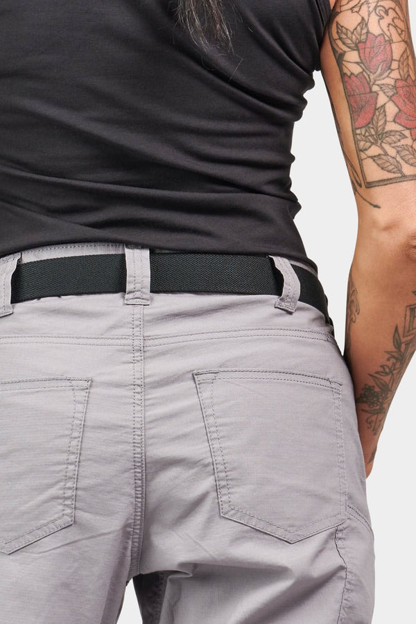 Back view of a woman wearing Dovetail Workwear's Flex Work Belt in Black, featuring a double-pronged buckle and elastic back design visible at the waistband of light gray pants
