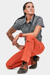 Woman crouching while wearing Dovetail Workwear's Anna Taskpant in Paprika Canvas, showcasing the reinforced knees, nested pockets, and Hip Slot™ Tool loop detail