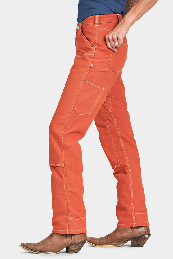 Side view of a woman wearing Dovetail Workwear's Anna Taskpant in Paprika Canvas, featuring reinforced knees, nested pockets, and contrast stitching.