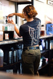 Back view of a woman wearing the Rae Ripple x Dovetail Workwear Brave Wings T-Shirt in black, featuring signature wings design across the back and relaxed fit 100% cotton construction.