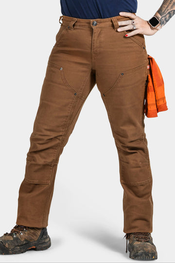 Britt Utility Pant in Saddle Brown Canvas by Dovetail Workwear shown on a woman wearing hiking boots, featuring reinforced knees, nested pockets, and a tool loop
