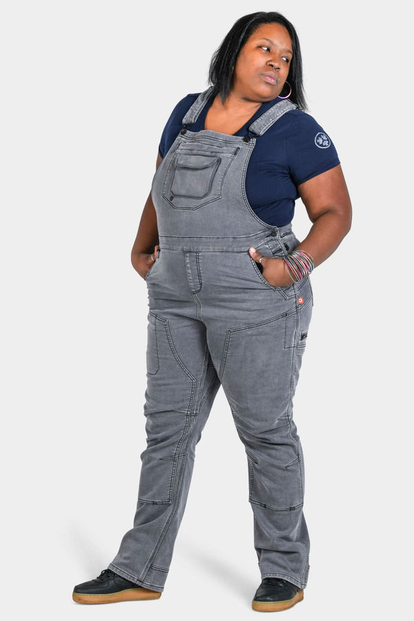 Freshley Drop Seat Overalls in Grey Stretch Thermal Denim by Dovetail Workwear, shown on a woman wearing a navy t-shirt, featuring reinforced knees and multiple pockets