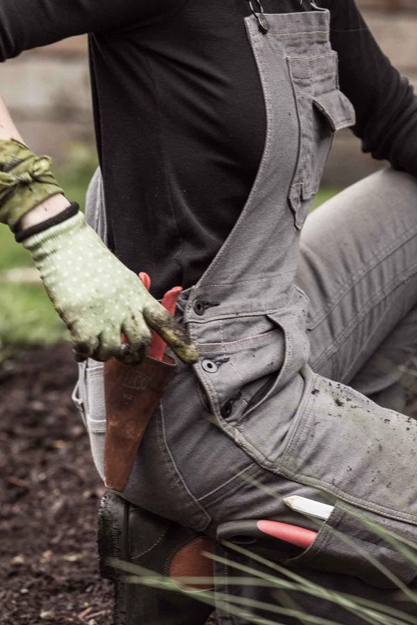 Woman gardening in grey canvas Freshley Overalls by Dovetail Workwear, showing reinforced knees and nested pockets while digging soil