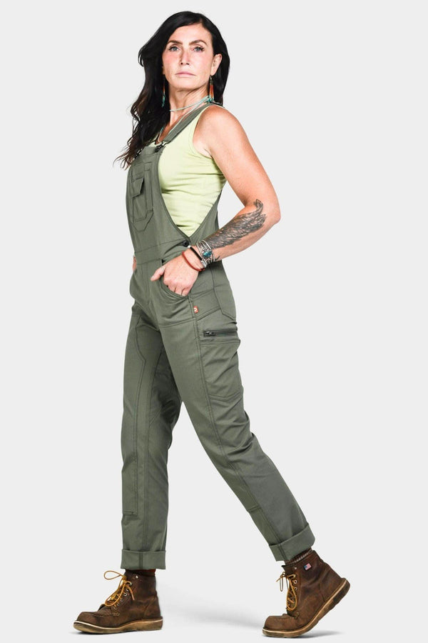 Side view of a woman wearing Dovetail Workwear's Freshley Overalls in Lichen Green Ultralight Ripstop, featuring flex suspenders and reinforced front with Tough Cuff™ rolled cuffs