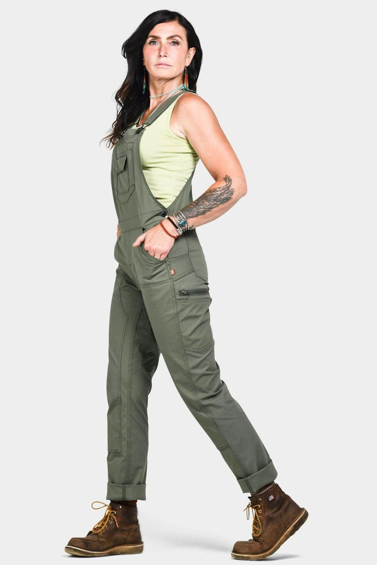 Side view of a woman wearing Dovetail Workwear's Freshley Overalls in Lichen Green Ultralight Ripstop, featuring flex suspenders and reinforced front with Tough Cuff™ rolled cuffs