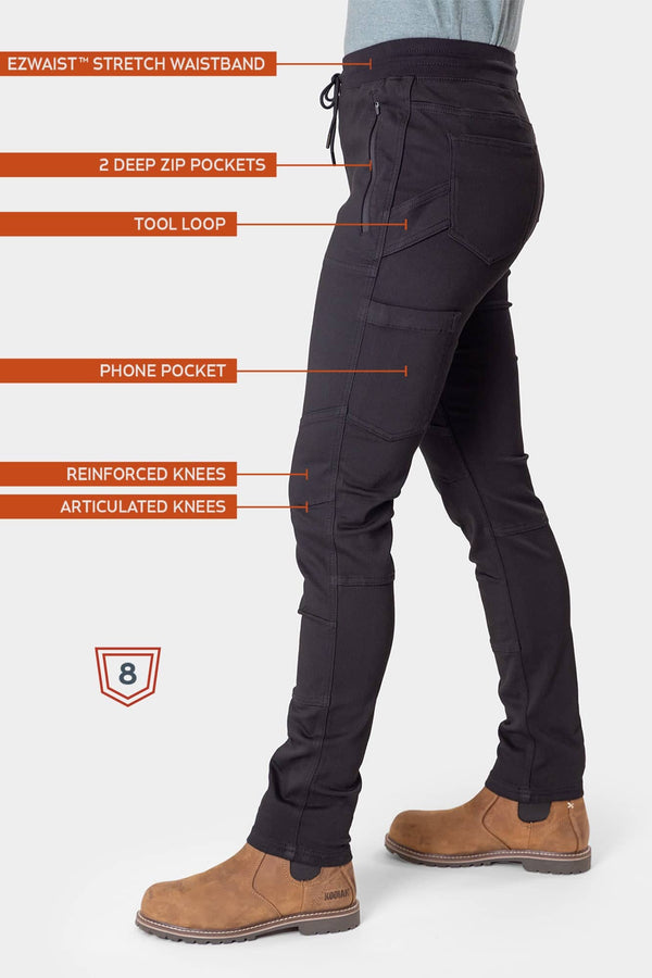 Side view of a woman wearing the Christa X DIY Pant in Black Performance Modal by Dovetail Workwear, highlighting the EZWaist stretch waistband, deep zip pockets, tool loop, phone pocket, and reinforced articulated knees