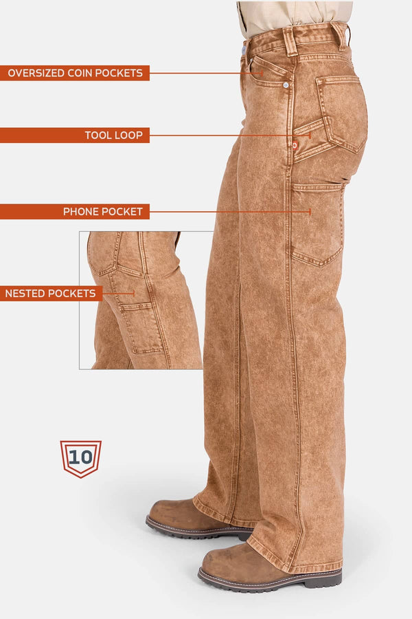 Side view of a woman wearing Dovetail Workwear's Old School Wide Leg Mineral Wash Jeans in Sunbaked Copper, highlighting nested side pockets, oversized coin pockets, tool loop, and phone pocket.