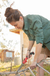 Woman wearing Aventurine Green AJ COOLSWAP™ Work Shirt by Dovetail Workwear while pruning branches, demonstrating the shirt's durability and mobility during outdoor gardening work