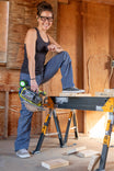 Woman wearing Dovetail Workwear Day X COOLSWAP™ Pant in Dovetail Blue, using a circular saw at a workbench in a workshop setting