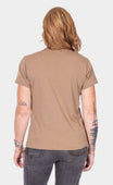 Back view of a woman wearing the Rae Ripple x Dovetail Workwear You Will Be Art T-Shirt in Alloy Brown, showcasing the relaxed fit and left sleeve text detail