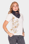 A woman wearing the Rae Ripple x Dovetail Workwear Brave Wings Bandana in black tied around her neck, paired with a cream tee featuring gold floral artwork