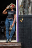 Woman wearing Dovetail Workwear's Get Dirty™ Crew Neck Tee in black, paired with jeans and work gloves, taking a water break on a job site