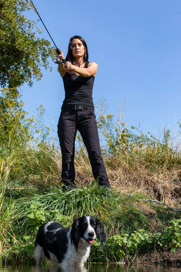 Woman fishing in Dovetail Workwear's GO TO™ Stretch Canvas Pant in Carbon Black, demonstrating the versatile work pant's comfort and functionality for outdoor activities
