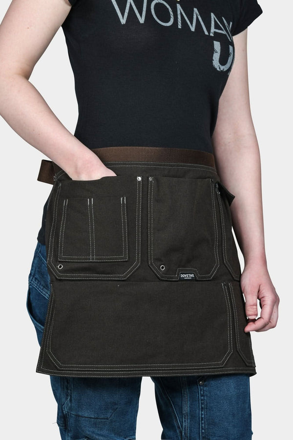 Dovetail Tool Apron in Kodiak Brown worn by a woman, showing multiple front pockets with contrast stitching, adjustable waist belt with quick release buckle, and dual hammer loops