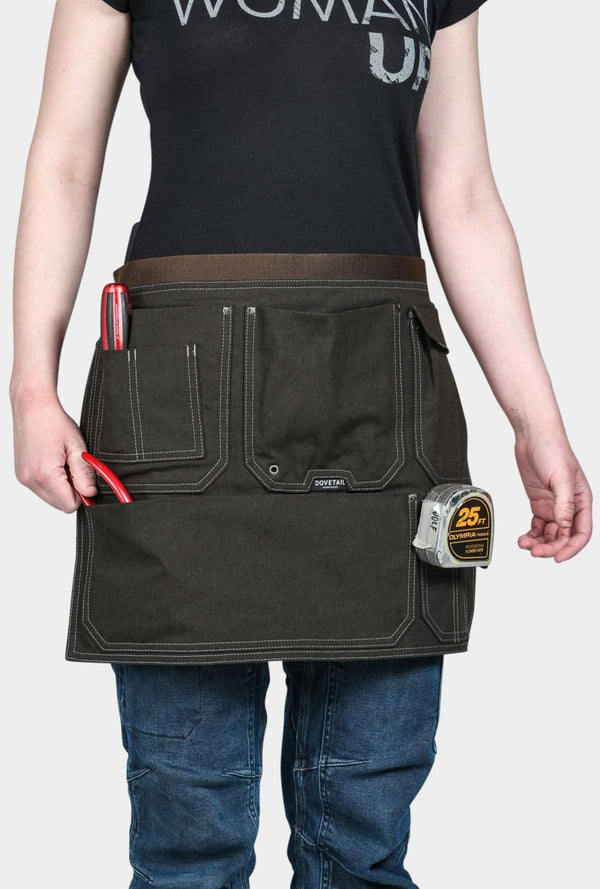 Dovetail Workwear Tool Apron in Kodiak Brown worn by a woman, displaying multiple pockets, hammer loops, and twine hole eyelets at the waist