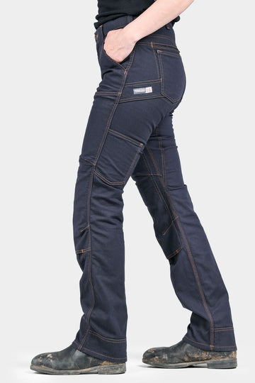 Side view of a woman wearing Dovetail Workwear's Britt Utility Pant in FR Navy Canvas, showcasing multiple cargo pockets, reinforced knees, and straight leg silhouette with work boots