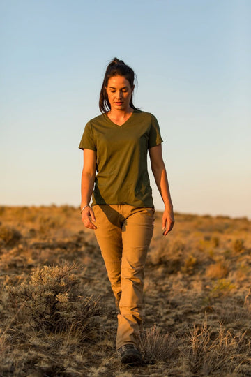 Woman walking across desert terrain wearing Dovetail Workwear GO TO™ Stretch Canvas Pant in Sawdust Brown with olive v-neck tee