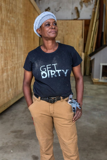 Woman wearing Dovetail Workwear's Flex Work Belt with double-pronged buckle, paired with tan work pants in an industrial setting