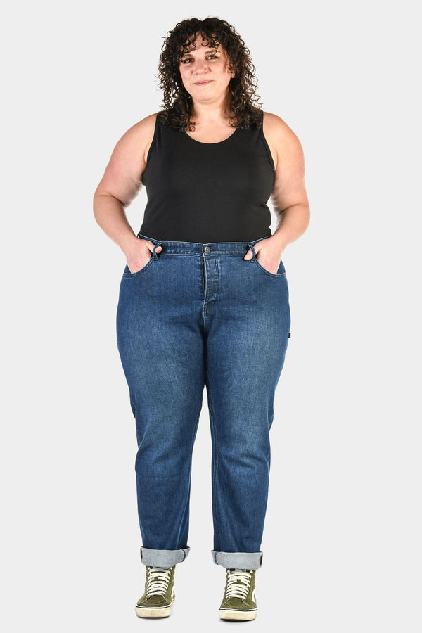 Pride Shop Pant in Indigo Denim Blue by Dovetail Workwear, shown on a woman wearing a black tank top and olive green high-top sneakers with cuffed inseams