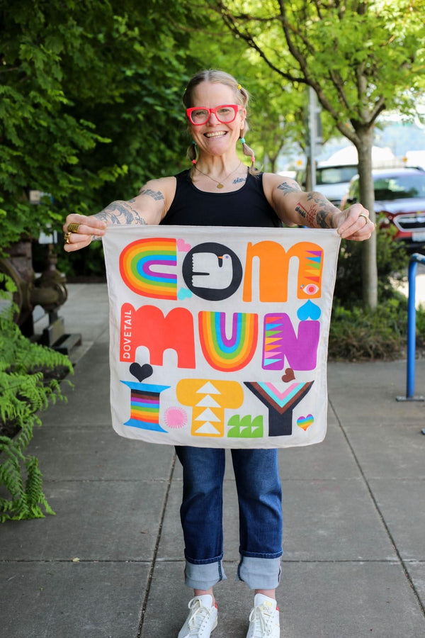 Woman holding Lisa Congdon's Pocket Pride Bandana by DoveLab™, displaying its vibrant rainbow colors and geometric designs inspired by the Progress Pride flag