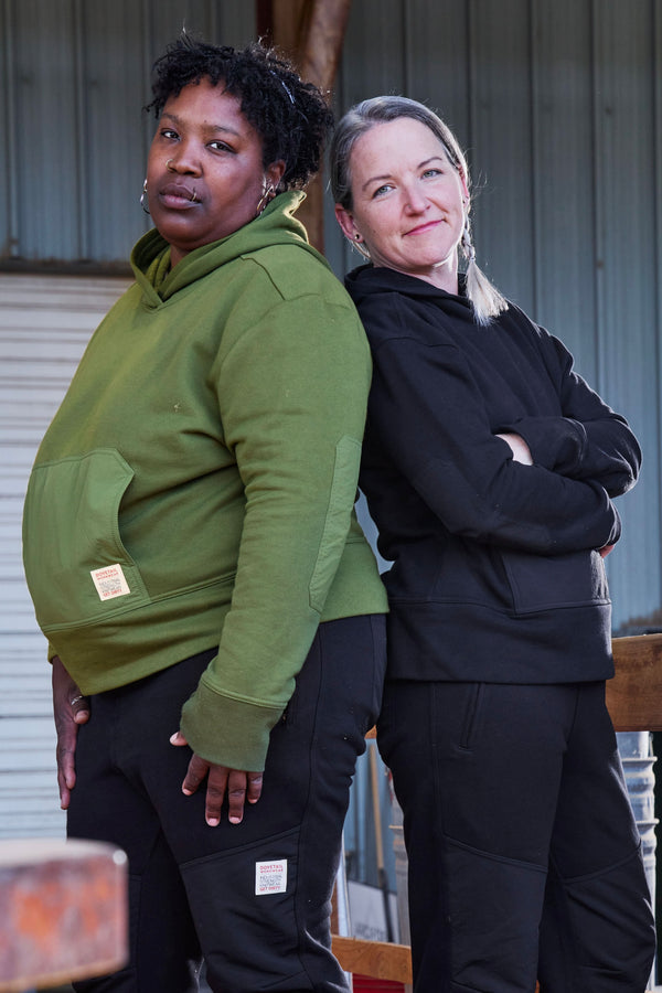 Two women modeling Dovetail Workwear's Flagger Fleece Hoodie in Moss Green, showcasing the reinforced front pocket and thumbhole cuffs from a front-facing angle