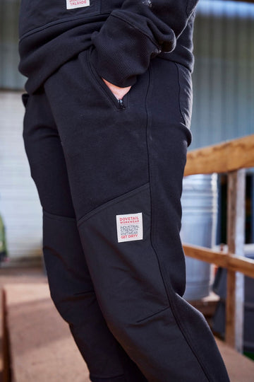 Side view of a woman wearing the Dovetail Workwear Flagger Fleece Jogger Work Pant in Black, showing reinforced knees and back pocket with brand label