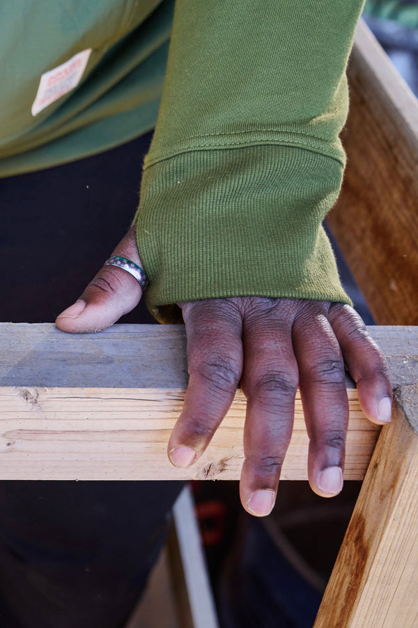 Detail shot of a woman's hand resting on wood while wearing the Moss Green Flagger Fleece Hoodie, showing the reinforced nylon elbow overlay