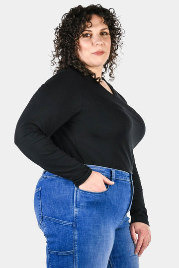 Side view of a woman wearing the Dovetail Workwear Long Sleeve V-Neck Tee in black with blue jeans, showcasing the relaxed fit and extra coverage