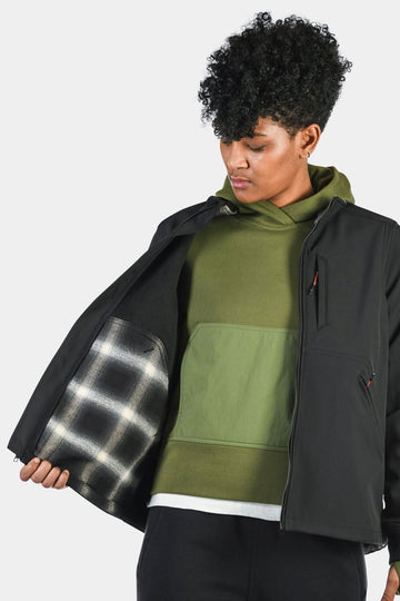 Side view of a woman wearing the M'fon Jacket in Black by Dovetail Workwear, with the jacket open to reveal the layered clothing and interior lining inside