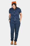 Dovetail Workwear's Hadley Short Sleeve Coveralls in Dark Blue Wabash Stripe, shown on a woman wearing brown boots and an orange cap, featuring reinforced knees and multiple pockets