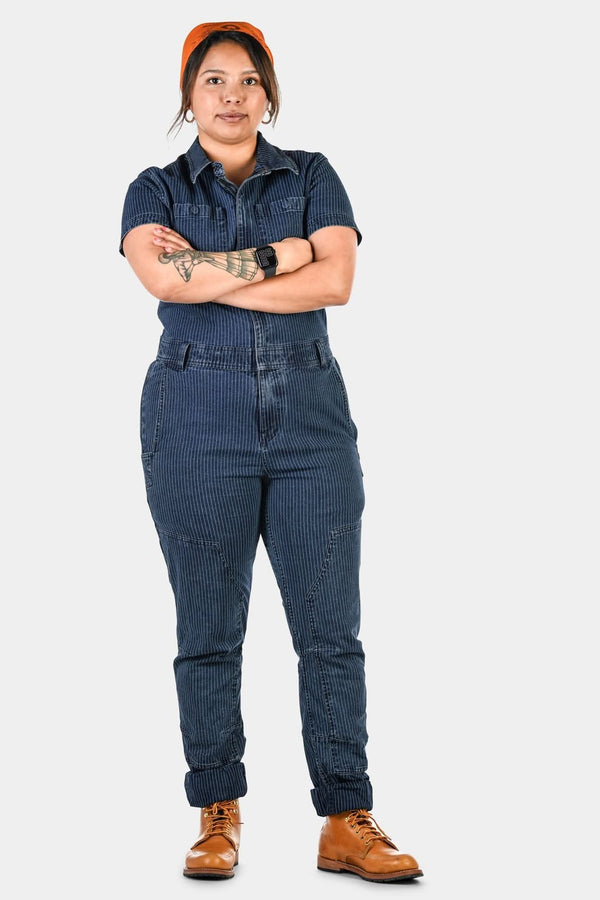 Woman wearing Dovetail Workwear Hadley Short Sleeve Coveralls in Dark Blue Wabash Stripe with arms crossed, showcasing reinforced knees and tool loop details